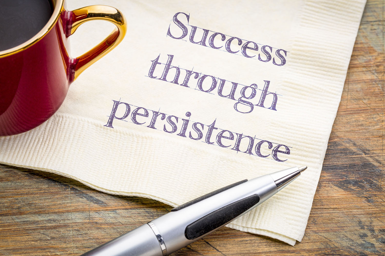 Success through persistence written on napkin next to cup of coffee.